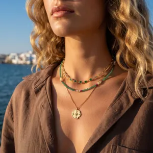 Close-up detail of layered gold necklaces featuring green stones and a star pendant outdoors.
