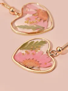Nahaufnahme herzförmiger Harzohrringe mit echten Trockenblumen in goldenem Rahmen.