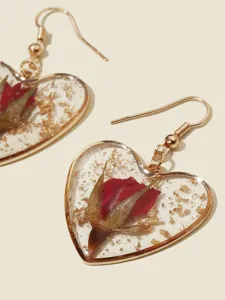 Nahaufnahme Detail herzförmiger Harzohringe mit getrockneter roter Rose und Goldfolienflocken.