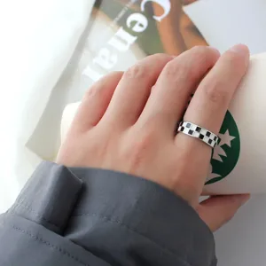 Close-up of a stylish black and white checkerboard ring worn on finger, modern aesthetic.