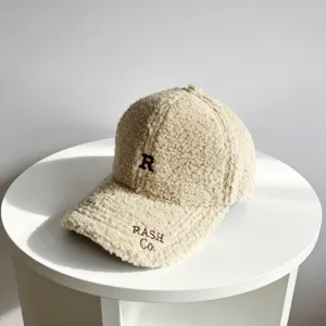Gros plan d'une casquette de baseball douillette en sherpa beige avec broderie marron.