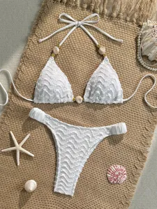 Close-up detail of white lace bikini set featuring elegant beaded charm straps and texture fabric.