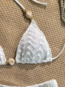 Detail shot of white textured lace bikini top with shell beads and chic gold accents.