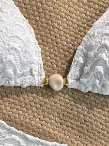 White lace bikini top detail featuring a natural shell and gold beads accent for beachwear.