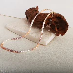 Gros plan détaillé d'un collier de perles d'eau douce dégradé sur bois flotté et pierre.