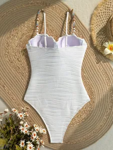 Dettaglio del costume intero bianco con tessuto ondulato e spalline con perline.