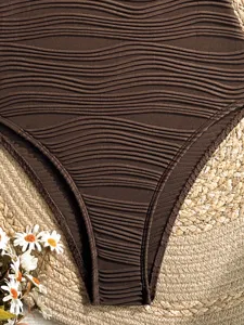 Primo piano dettaglio di slip bikini a coste marrone su sfondo di paglia intrecciata.
