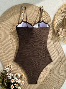 Dettaglio costume da bagno intero marrone testurizzato con spalline di perle e onde.