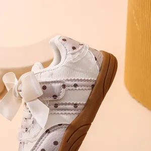 Primo piano sui dettagli di sneaker per bambina con fiocco bianco e pois su morbida suola marrone.