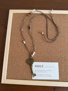 Primo piano dettagliato della collana con ciondolo chiave a cuore, corda intrecciata e perle.