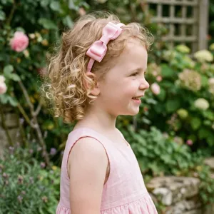 Closeup view of the cute pink grosgrain ribbon bow headband worn by a child outdoors, detail.