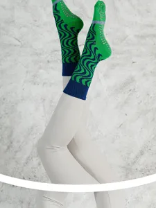 Close-up of green and blue wave pattern grip socks worn on legs for yoga and pilates fitness.