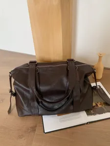 Detailed shot of dark brown travel duffel bag showcasing leather texture, dual handles and strap.