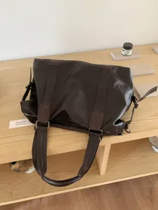 Close-up view of a dark brown faux leather travel tote bag placed on a wooden shelf.