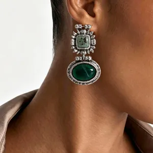 Gros plan de boucles d'oreilles pendantes style baroque vintage en métal argenté et pierres vertes.