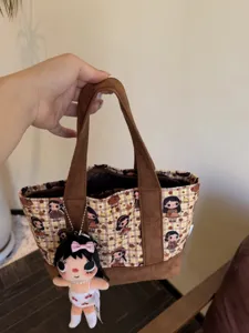 Detailed view of cute canvas tote bag with cartoon girl pattern and doll pendant.