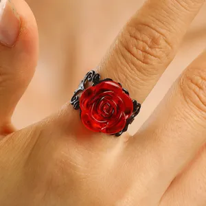 Close-up detail of the red resin rose ring with black filigree metal base on finger.