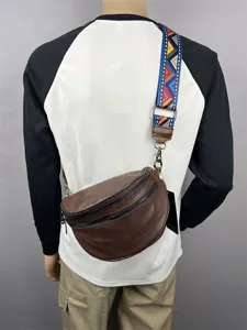 Detail shot of brown leather sling bag with colorful ethnic pattern strap and metal zippers.