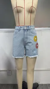 Detailed view of women's high waist denim shorts with colorful daisy floral print and raw hem.