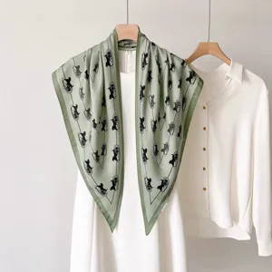 Vue détaillée de l'élégant foulard en soie vert à motif de calèche avec robe blanche.