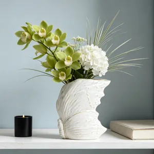 Moderno vaso in ceramica bianca con ali di farfalla nordico con composizione floreale artificiale.