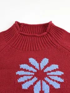 Close-up view of the ribbed collar and blue knitted flower pattern on red sweater fabric.