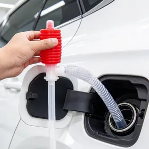 Hand squeezes a red siphon pump as its clear hose is inserted into a car's fuel tank
