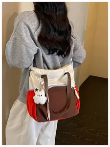 Vue de dos d’un modèle portant un sac crème, brun et rouge avec un porte-clés ours en peluche