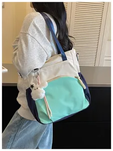Une personne porte un sac écru, vert menthe et bleu marine avec un porte-clés ours en peluche