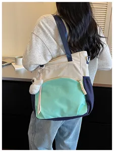 Vue de côté du sac crème et menthe porté, avec bordure bleu marine et pendentif en peluche