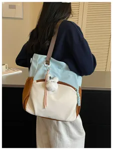 Vue de côté d’un modèle portant un sac bicolore à bordure brune avec un pendentif ourson en peluche