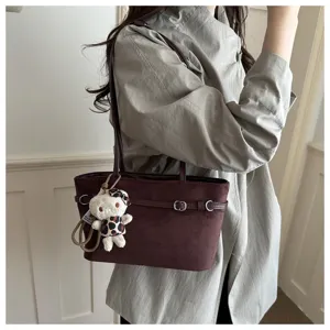 Una persona porta una borsa in suede marrone caffè, con fibbie argentate e un orsetto pendente