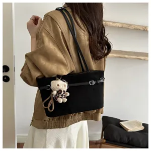 Una donna indossa una borsa nera a spalla, con cinturino a fibbia e un piccolo ciondolo a forma di orsetto