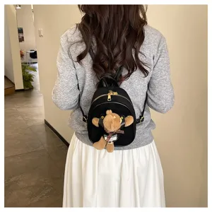 Rear view of a model wearing a mini black suede backpack with gold zipper and brown plush bear charm