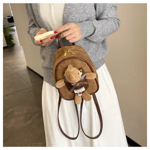 Close-up of a brown suede-look backpack with gold zippers and a teddy bear charm with a plaid bow
