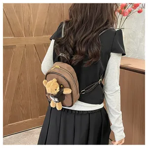 Back view of a model wearing a brown suede backpack with a teddy bear charm and gold zipper