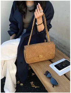 Close-up of a brown quilted bag with suede-like texture and a gold chain strap on a bench