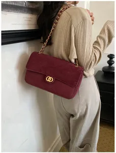 Back view of a model carrying a burgundy suede flap bag with a gold chain and ring clasp.