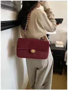 Woman wearing a burgundy quilted flap bag with gold chain strap, shown in a relaxed indoor setting