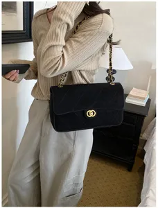 A black quilted flap bag with a gold chain strap and clasp, carried over a beige sweater