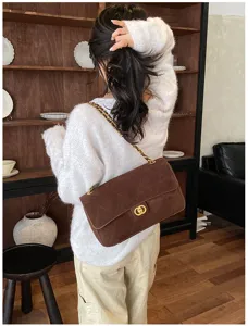 Detail of a brown suede-look flap bag with gold chain strap and turn-lock clasp, worn on the shoulder