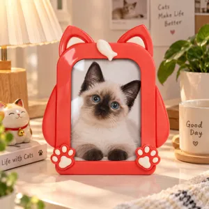 Red cat-shaped photo frame with paw and fish details, displayed on a table with a cat portrait