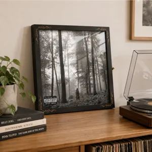 Album cover displayed behind glass in a black frame with orange trim, styled beside a turntable