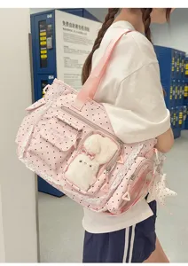 Vue de profil du sac rose à pois porté à l’épaule, avec bordure en dentelle et poches transparentes