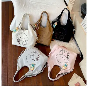 Cinq sacs en toile crème, beige, noir, gris et rose, ornés de motifs de chiens et de breloques colorées sur le lit