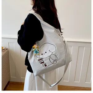 Une personne porte dans le dos un sac gris clair à motif de chien avec un petit pendentif décoratif