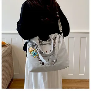 Modèle portant en intérieur un sac gris clair avec ours imprimé, bandoulière rayée et breloque