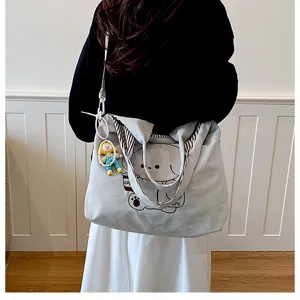 Vue de dos d’une personne portant un sac gris clair, imprimé ours, doublure rayée et breloque