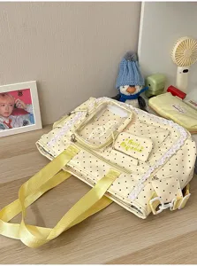 Détail d’un sac crème à pois noirs, avec bordure en dentelle, poche transparente et anses jaunes