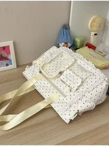 Détail d’un sac blanc à pois noirs, bordure en dentelle, poche transparente et anses beiges